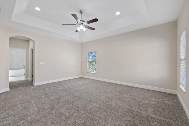 carpeted empty room with arched walkways, recessed lighting, a raised ceiling, and baseboards