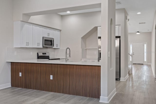 kitchen with stainless steel appliances, tasteful backsplash, visible vents, a sink, and a peninsula