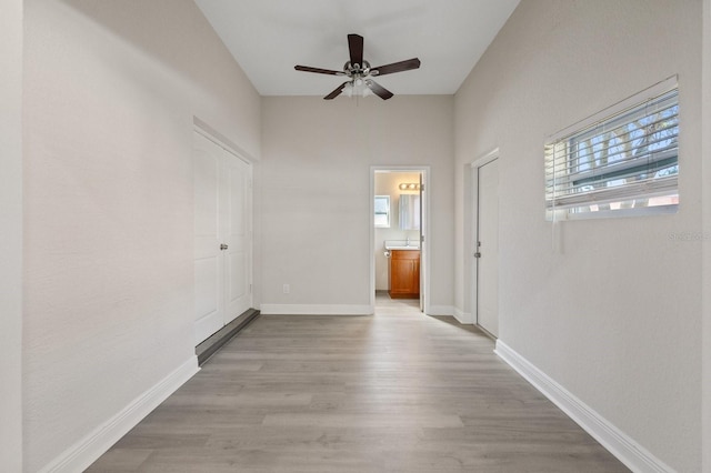 empty room with ceiling fan, light wood finished floors, and baseboards