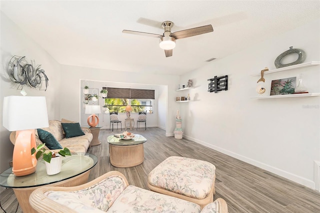 living room with a ceiling fan, visible vents, baseboards, and wood finished floors