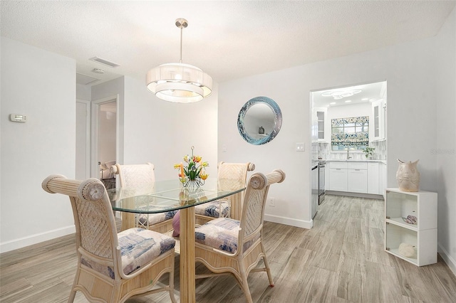 dining space with light wood-style floors, visible vents, baseboards, and a textured ceiling