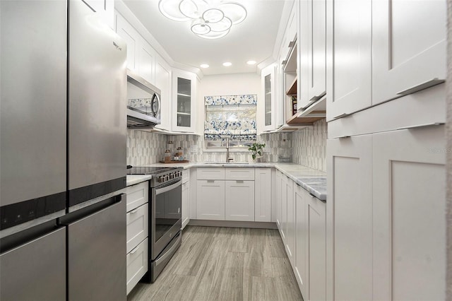 kitchen with white cabinets, decorative backsplash, glass insert cabinets, appliances with stainless steel finishes, and a sink