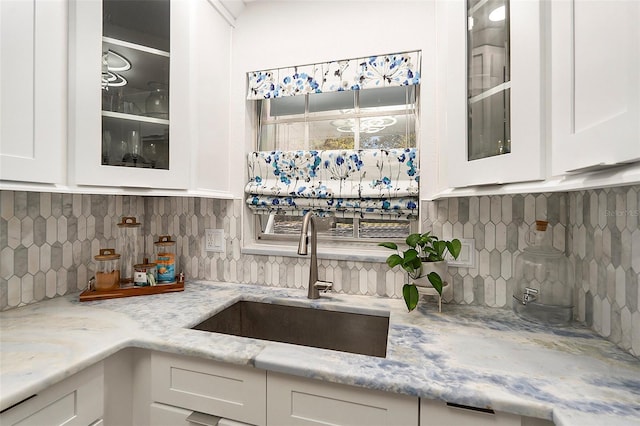 kitchen with glass insert cabinets, white cabinetry, light stone counters, and a sink