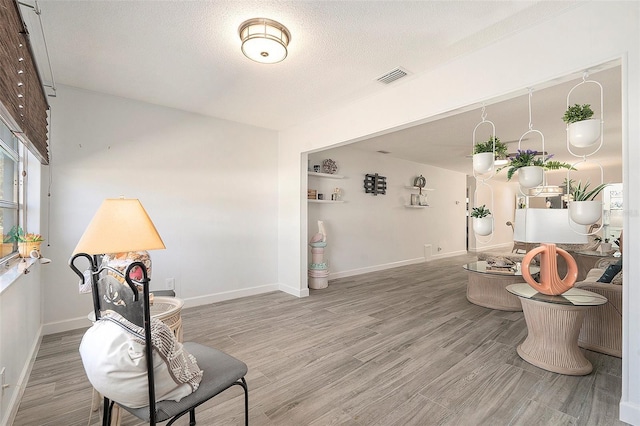 sitting room with visible vents, a textured ceiling, baseboards, and wood finished floors