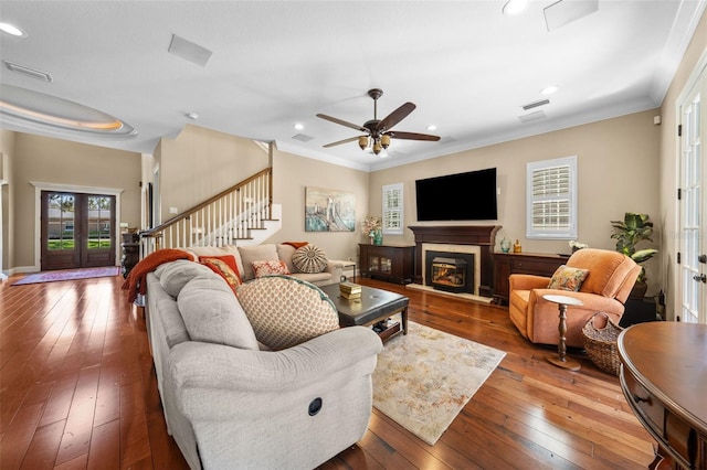 living area featuring ornamental molding, a glass covered fireplace, stairway, and hardwood / wood-style flooring