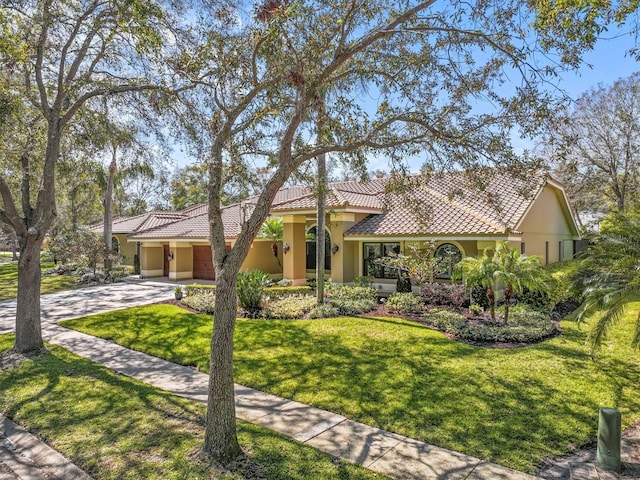 mediterranean / spanish-style home with an attached garage, driveway, a tiled roof, stucco siding, and a front yard