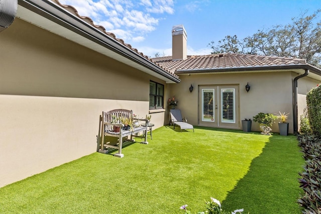 back of property with french doors, a chimney, stucco siding, a lawn, and a tiled roof