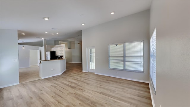 unfurnished living room featuring light wood-type flooring, a sink, recessed lighting, baseboards, and lofted ceiling