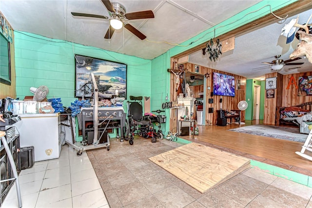 interior space with ceiling fan, wood walls, tile patterned flooring, and concrete block wall