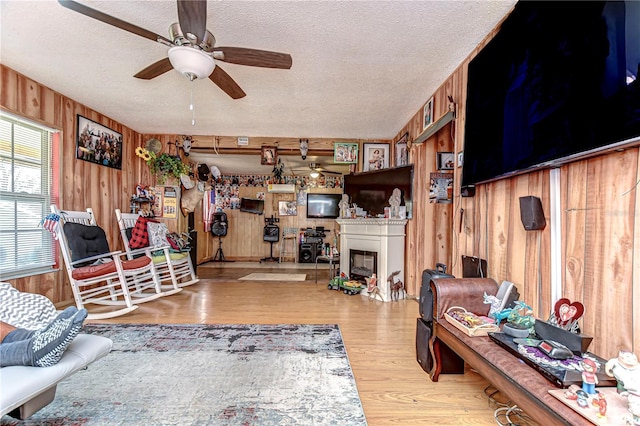 living room featuring a textured ceiling, ceiling fan, wood walls, a fireplace, and wood finished floors