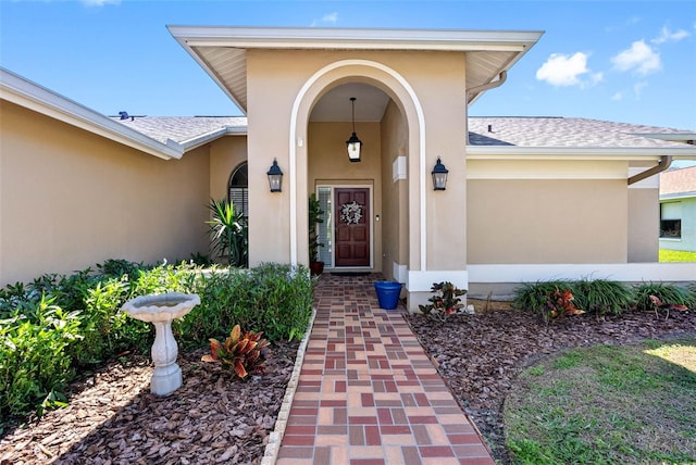 entrance to property featuring a shingled roof and stucco siding