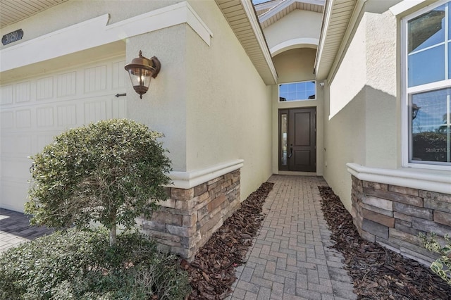 property entrance featuring stone siding, an attached garage, and stucco siding