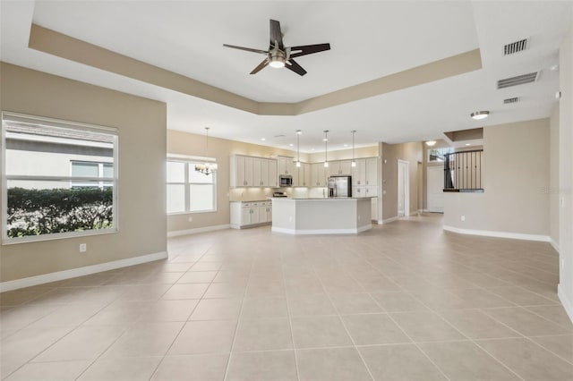 unfurnished living room featuring ceiling fan with notable chandelier, a tray ceiling, visible vents, and baseboards