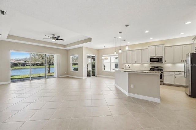 kitchen with a tray ceiling, light tile patterned floors, a water view, appliances with stainless steel finishes, and open floor plan