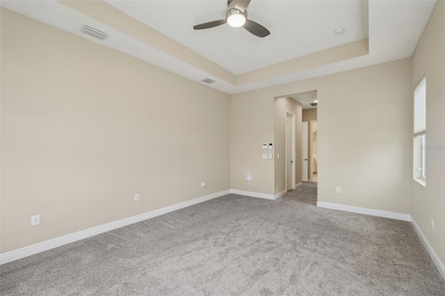 carpeted spare room featuring baseboards, visible vents, ceiling fan, and a tray ceiling