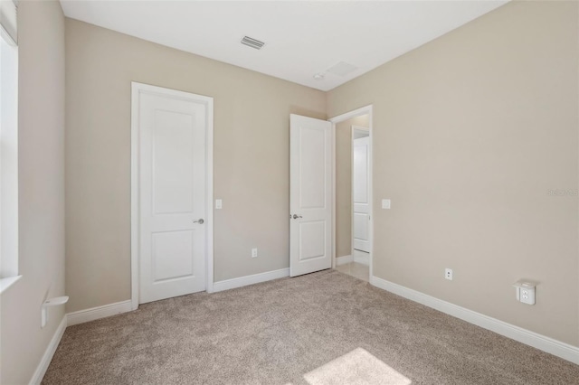 unfurnished bedroom featuring visible vents, light carpet, and baseboards