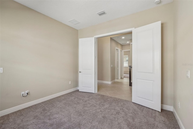 empty room featuring light carpet, light tile patterned floors, visible vents, and baseboards