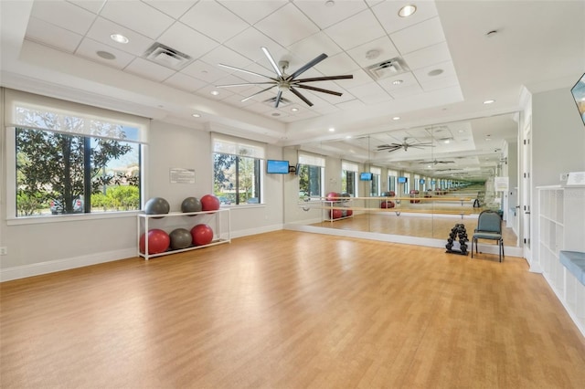 exercise room with baseboards, visible vents, a ceiling fan, wood finished floors, and a tray ceiling