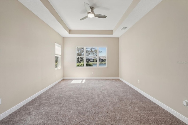 carpeted empty room with ceiling fan, a raised ceiling, visible vents, and baseboards