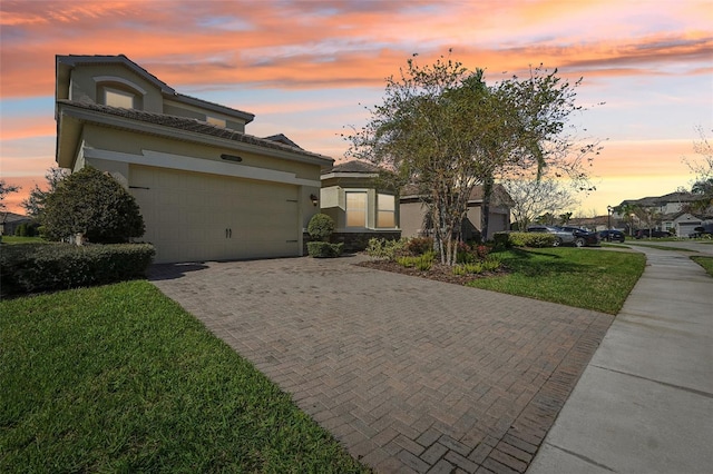 view of front of property featuring an attached garage, a yard, decorative driveway, and stucco siding