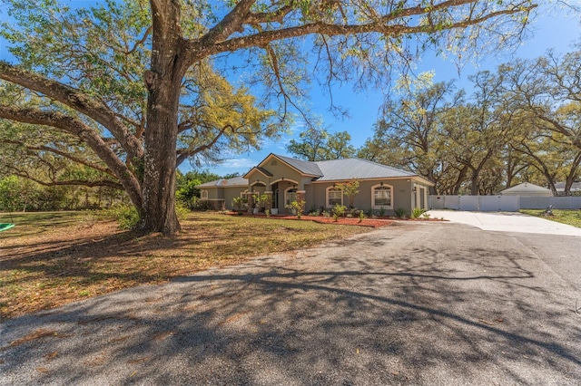 view of front of home featuring stucco siding, driveway, metal roof, and fence