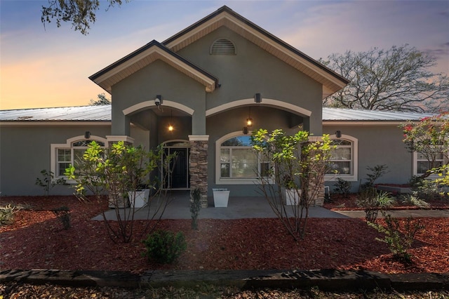 view of front of home with stone siding, stucco siding, and metal roof