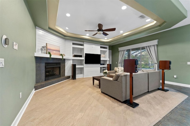 living area with visible vents, baseboards, a tiled fireplace, wood finished floors, and a raised ceiling