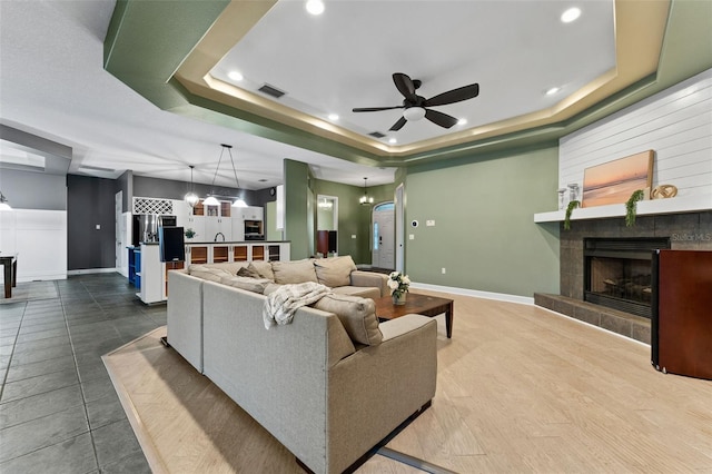 living room with a tray ceiling, baseboards, visible vents, and a fireplace