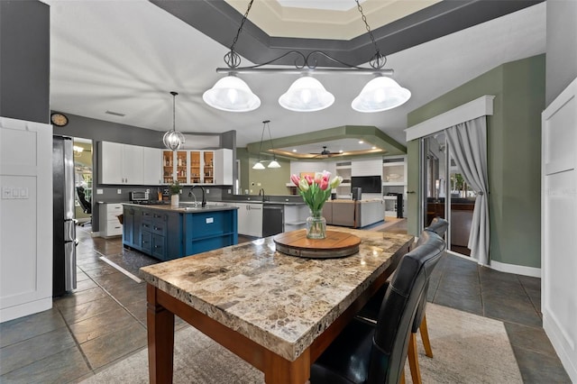 kitchen with a kitchen island with sink, blue cabinetry, white cabinetry, freestanding refrigerator, and baseboards