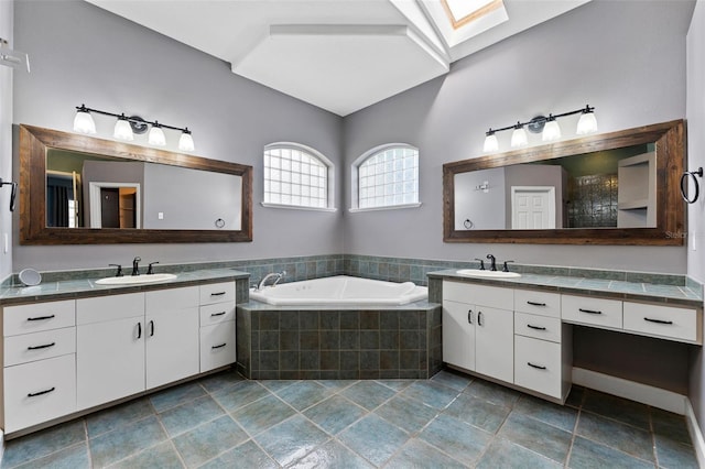 bathroom featuring a sink, vaulted ceiling with skylight, a garden tub, and two vanities