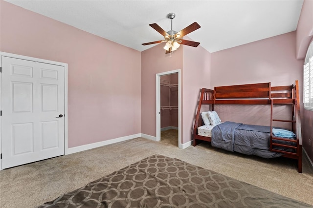 carpeted bedroom featuring a walk in closet, a closet, baseboards, ceiling fan, and vaulted ceiling