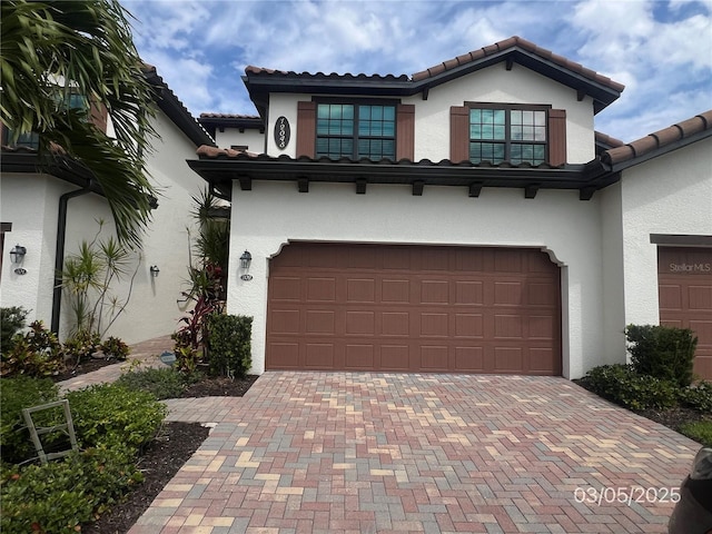 mediterranean / spanish home featuring a garage, decorative driveway, a tile roof, and stucco siding