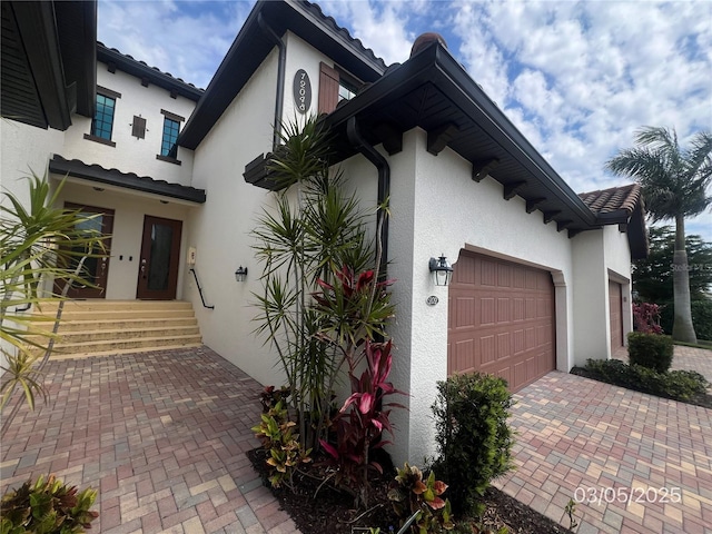 exterior space with an attached garage, a tile roof, decorative driveway, and stucco siding