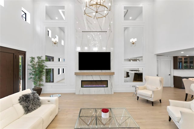 living room with a notable chandelier, wood finished floors, a high ceiling, and a glass covered fireplace