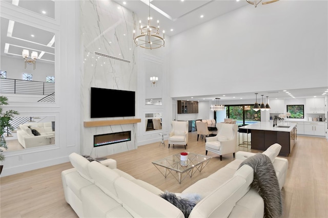 living area with an inviting chandelier, a fireplace, light wood-type flooring, and a towering ceiling