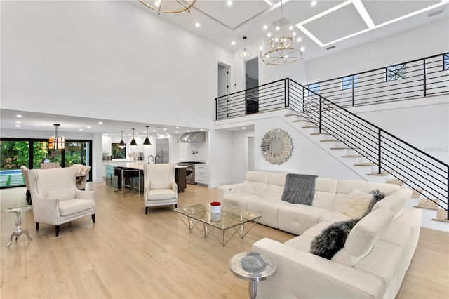 living area featuring visible vents, a high ceiling, light wood finished floors, a chandelier, and stairs