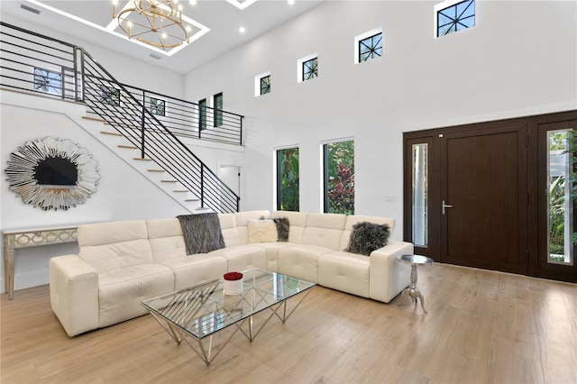 living room featuring a towering ceiling, a chandelier, stairs, and light wood finished floors