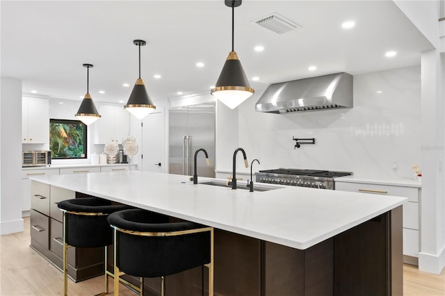 kitchen with visible vents, a sink, stainless steel built in fridge, light countertops, and wall chimney exhaust hood