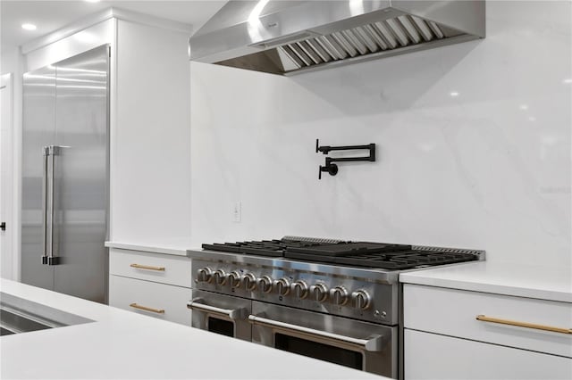 kitchen with light countertops, wall chimney range hood, high end appliances, and white cabinets