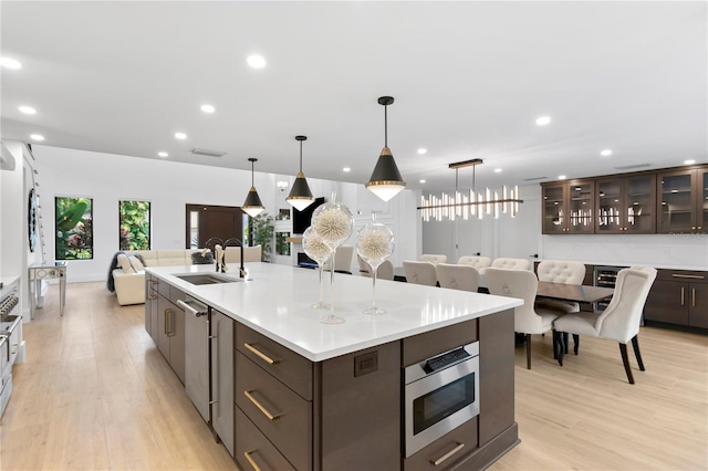 kitchen with dark brown cabinets, appliances with stainless steel finishes, light wood-style floors, a large island, and a sink