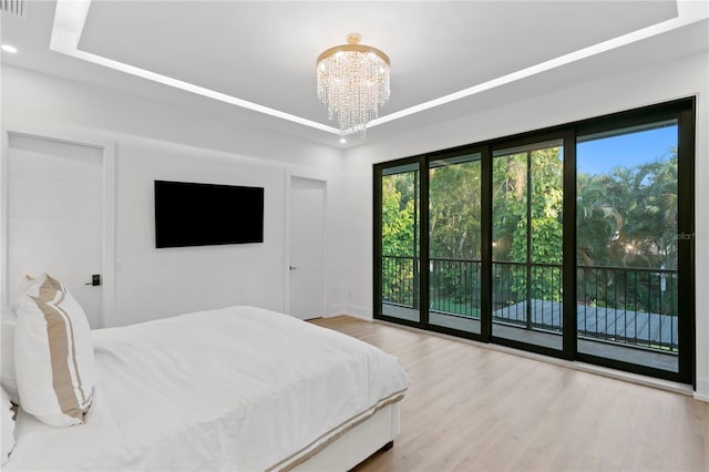 bedroom featuring access to exterior, a notable chandelier, a raised ceiling, and wood finished floors