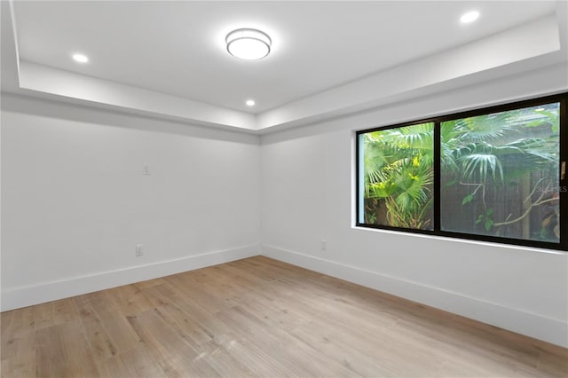 empty room featuring a tray ceiling, recessed lighting, baseboards, and light wood-type flooring