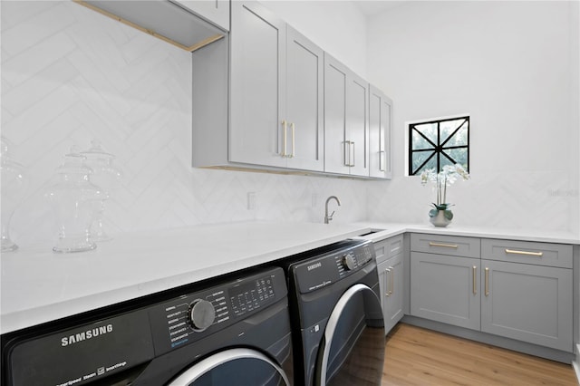 laundry room with cabinet space, washer and dryer, light wood-type flooring, and a sink