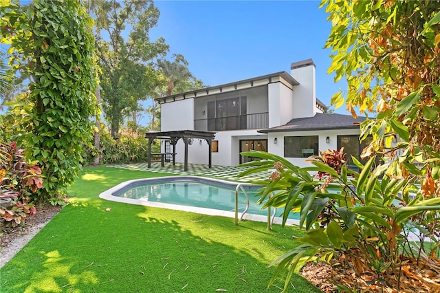 back of house featuring a lawn, stucco siding, a chimney, an outdoor pool, and a pergola