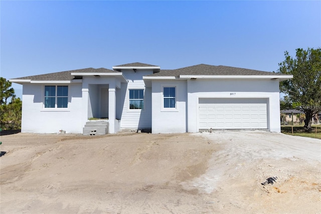 prairie-style home featuring driveway, roof with shingles, an attached garage, and stucco siding