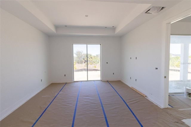 empty room featuring a tray ceiling, visible vents, and baseboards