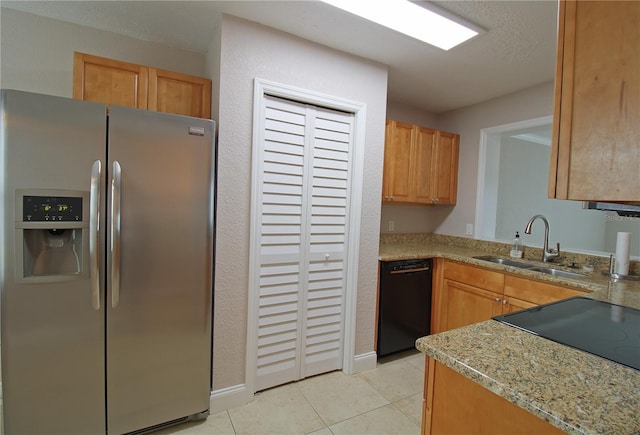 kitchen with light tile patterned floors, light stone counters, a sink, stainless steel refrigerator with ice dispenser, and dishwasher