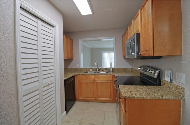 kitchen featuring light tile patterned floors, a textured wall, appliances with stainless steel finishes, brown cabinets, and a sink