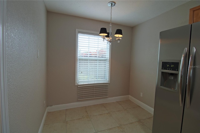 unfurnished dining area with light tile patterned floors, a textured wall, a chandelier, and baseboards