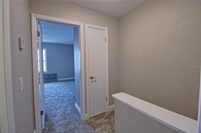 hallway featuring carpet flooring, a textured wall, a textured ceiling, and baseboards